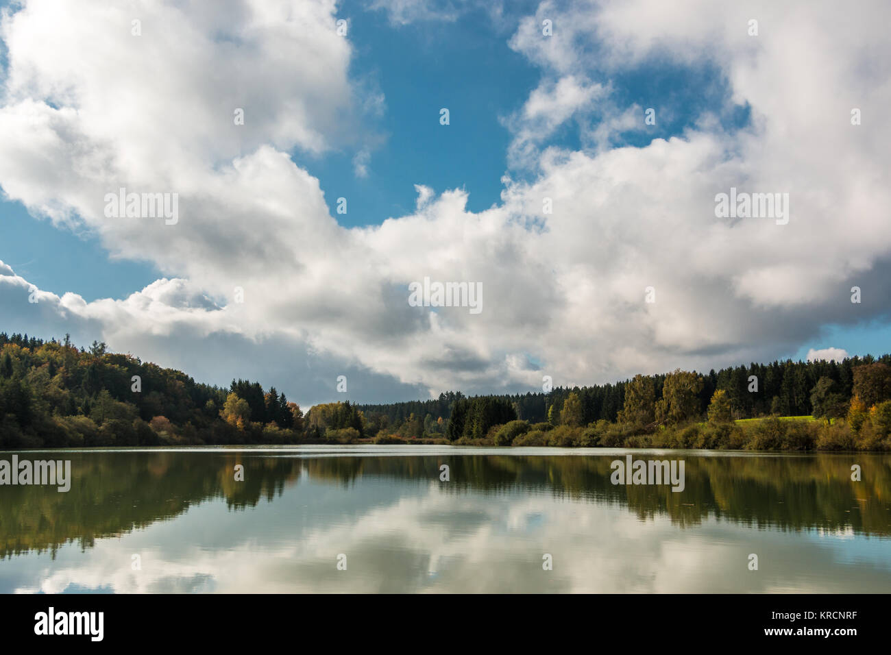 Lonely lago con riflessi nell'acqua e foreste attorno e cielo blu con nuvole Foto Stock