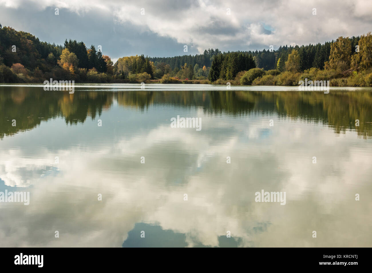 Lonely lago con riflessi nell'acqua e foreste attorno e cielo blu con nuvole Foto Stock
