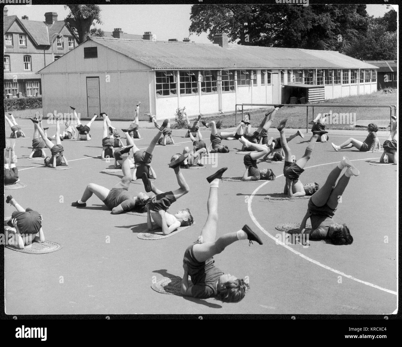 Ragazzi e ragazze si stendono sulla schiena su materassini e fanno esercizi alle gambe nel parco giochi come parte della loro lezione di P.E. Foto Stock