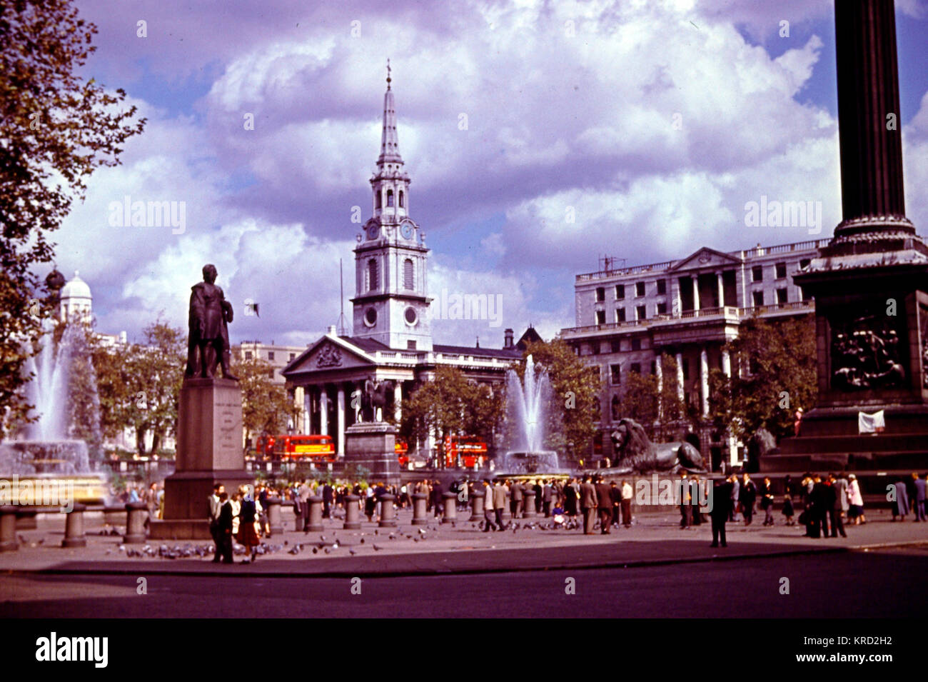 Una scena diurna a Trafalgar Square, Londra, con due fontane in azione, persone e piccioni, e la chiesa di St Martin in the Fields sullo sfondo. Foto Stock