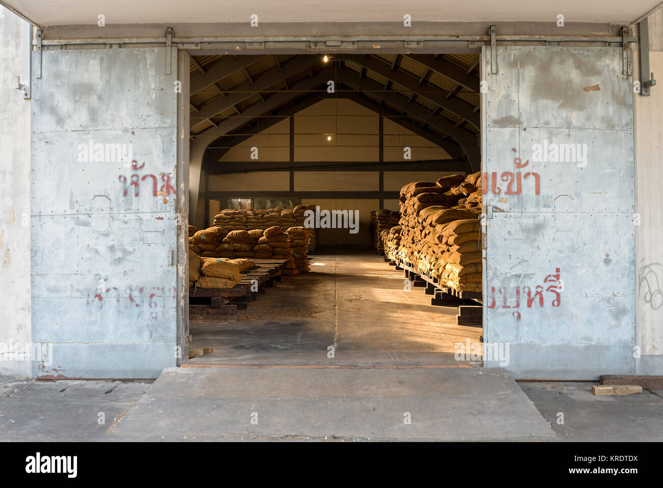 Impilati piena hessian sacchi in attesa di raccolta in un grande magazzino attraverso una porta aperta. Foto Stock