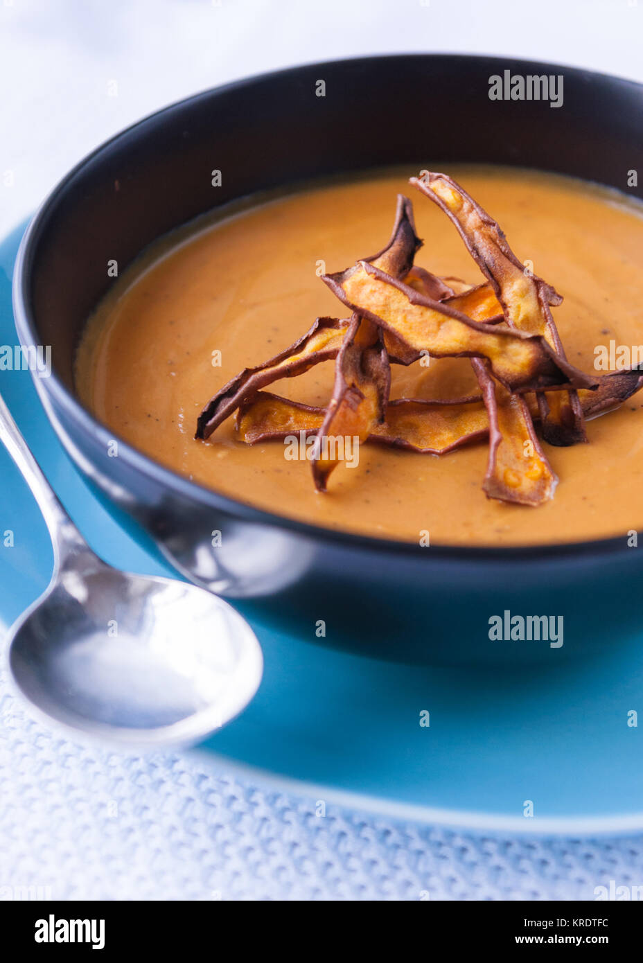 Dolce zuppa Potao carmelised con trucioli di carota in nero la coppa con piastra blu nastro cucchiaio su tovaglie bianche tovaglie Foto Stock