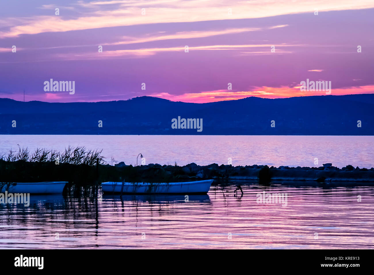Vivid Rosa tramonto sul lago calmo e silhouette di barche a remi. Sunrise colorati con piccole imbarcazioni al tranquillo lago di Balaton, Ungheria. Foto Stock