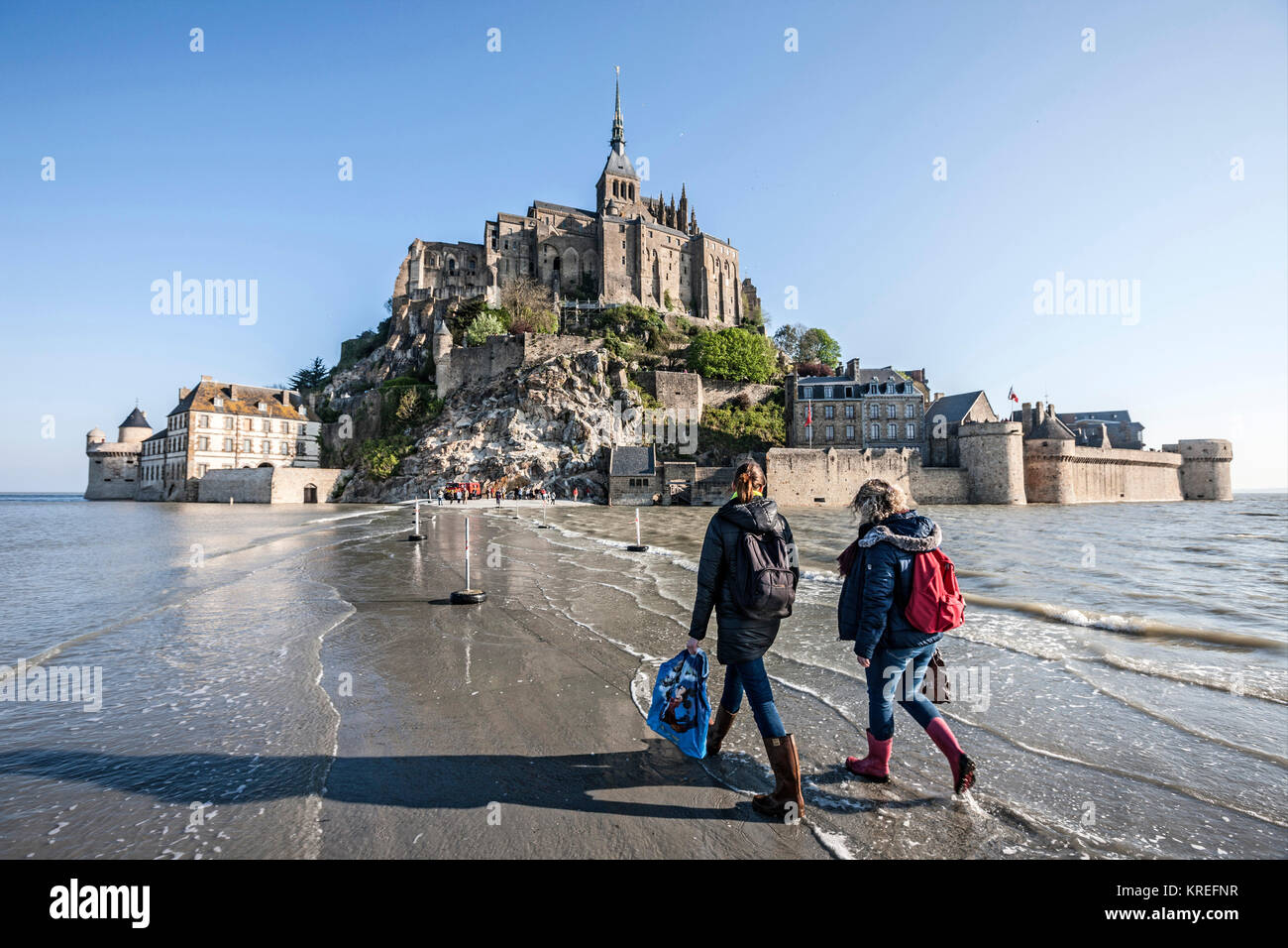 Mont Saint Michel (Saint Michael Mount), Normandia, a nord-ovest della Francia: Spring Tide di aprile, salendo sul mare. Due giovani donne visto da dietro il visitatore occasionale Foto Stock