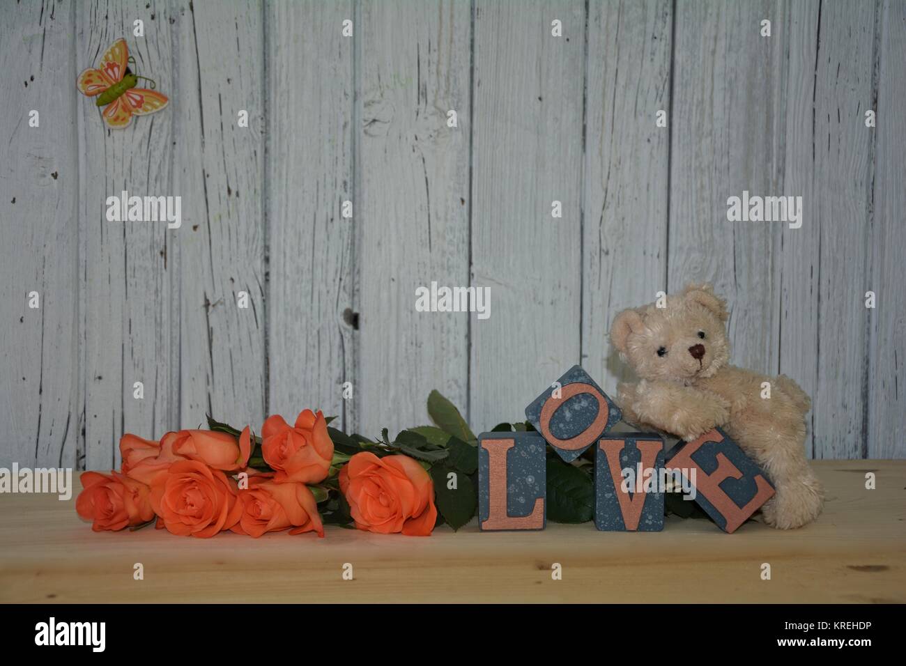 Orsacchiotto bianco giace sull amore di pietre contro la parete di legno con rose arancione Foto Stock