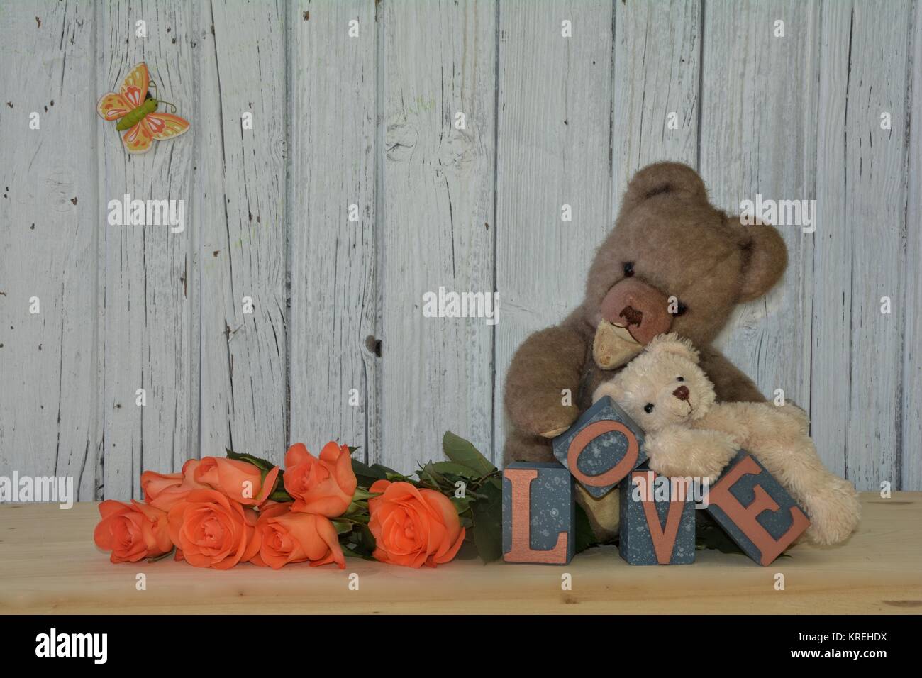 Due orsacchiotti con rose e amore scritte contro bianco parete in legno Foto Stock