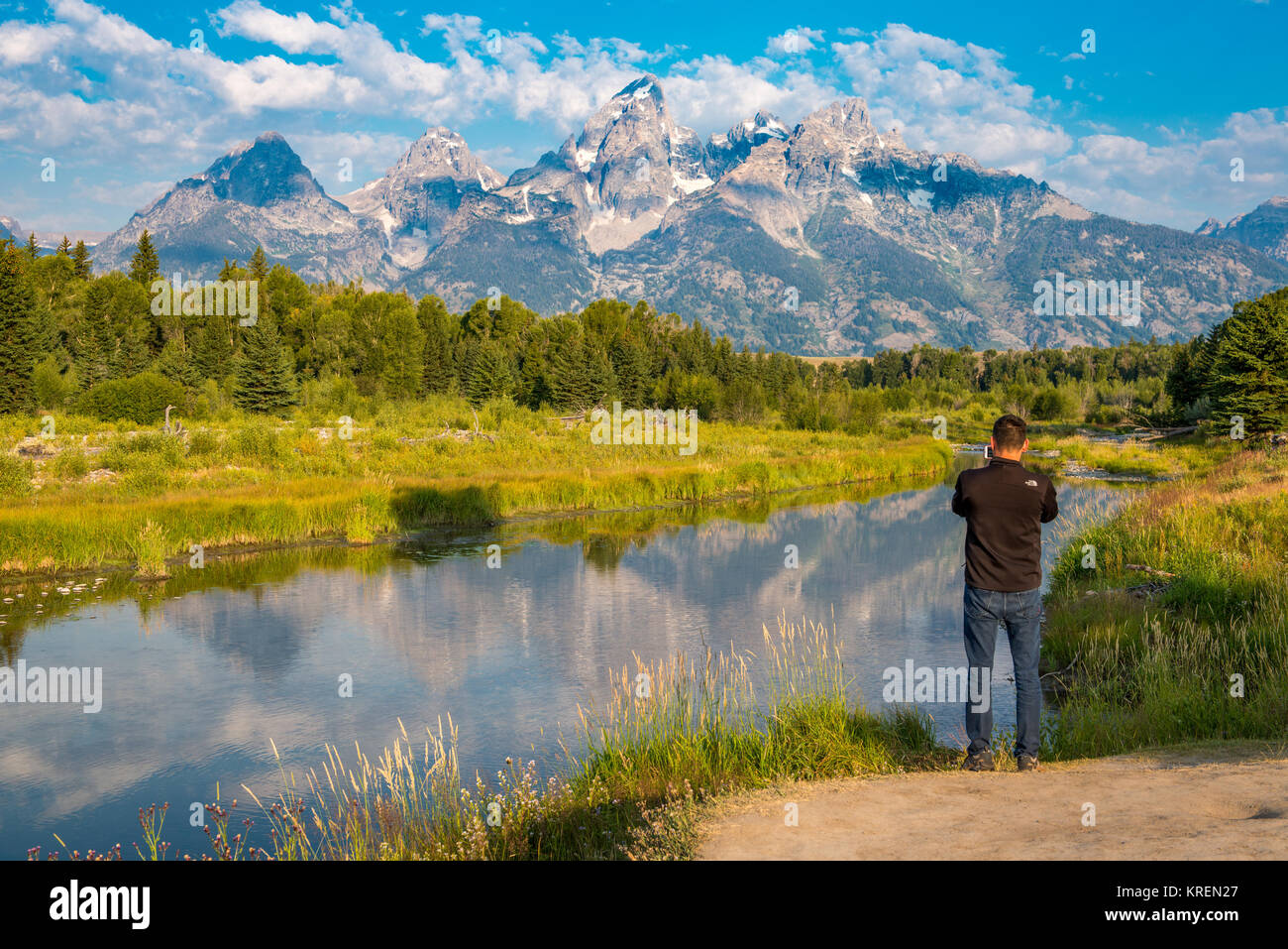 Giovani maschi adulti si erge a bordo del fiume Snake e utilizza il cellulare per scattare foto di Teton Mountain Range, Grand Tetons National Park, Teton County, Wyo Foto Stock