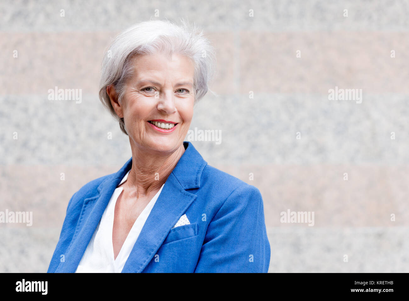 Lächelnde Seniorin mit grauem Haar vor einer Wand Foto Stock
