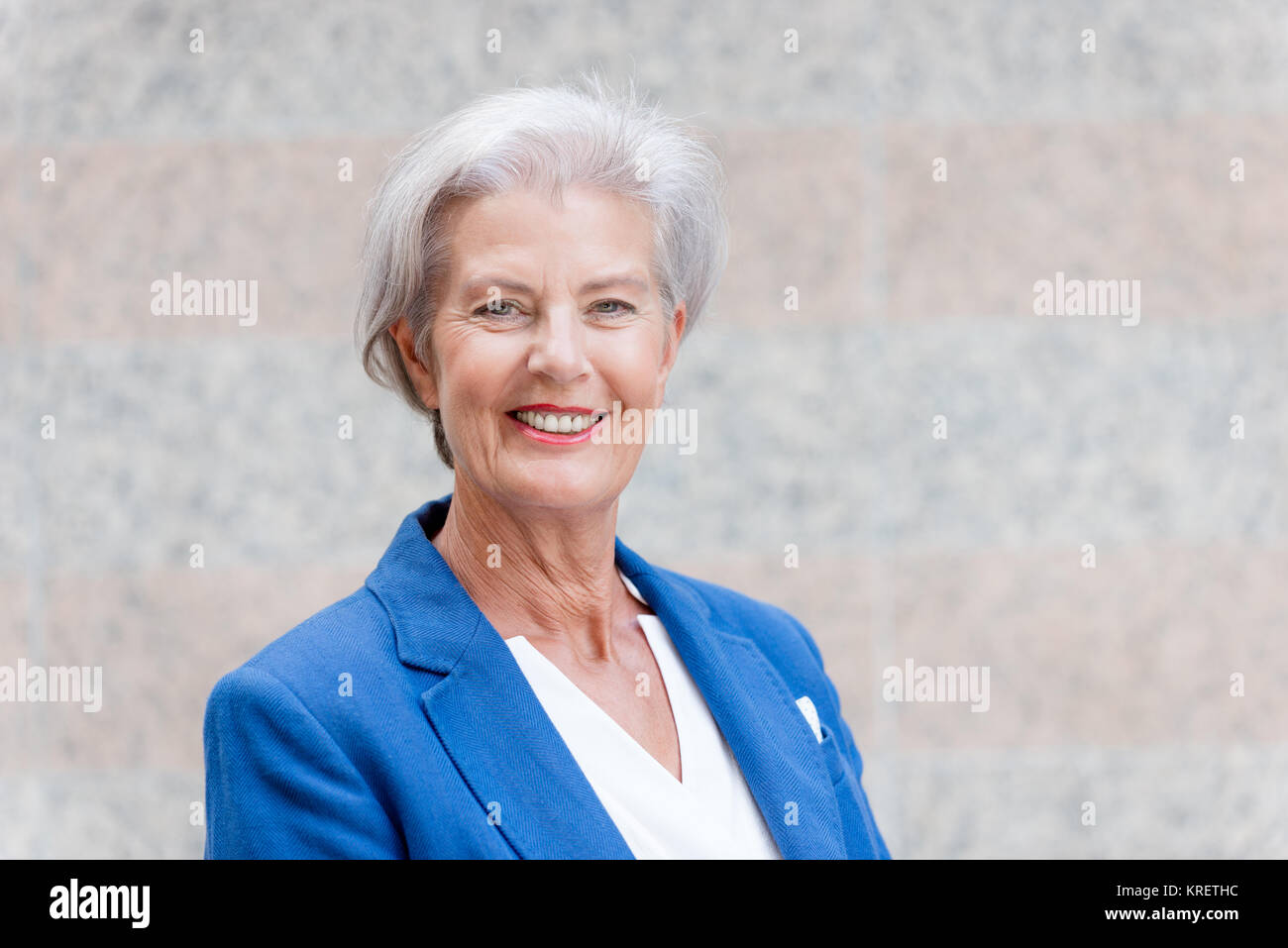 Lächelnde Seniorin mit grauem Haar vor einer Wand Foto Stock