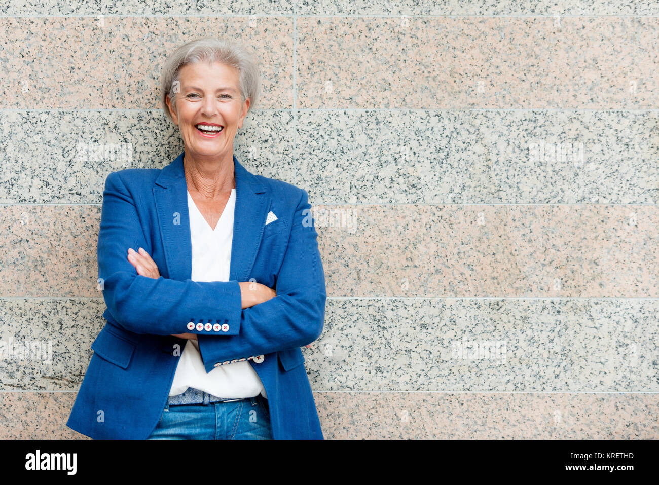 Lächelnde Seniorin mit grauem Haar vor einer Wand Foto Stock