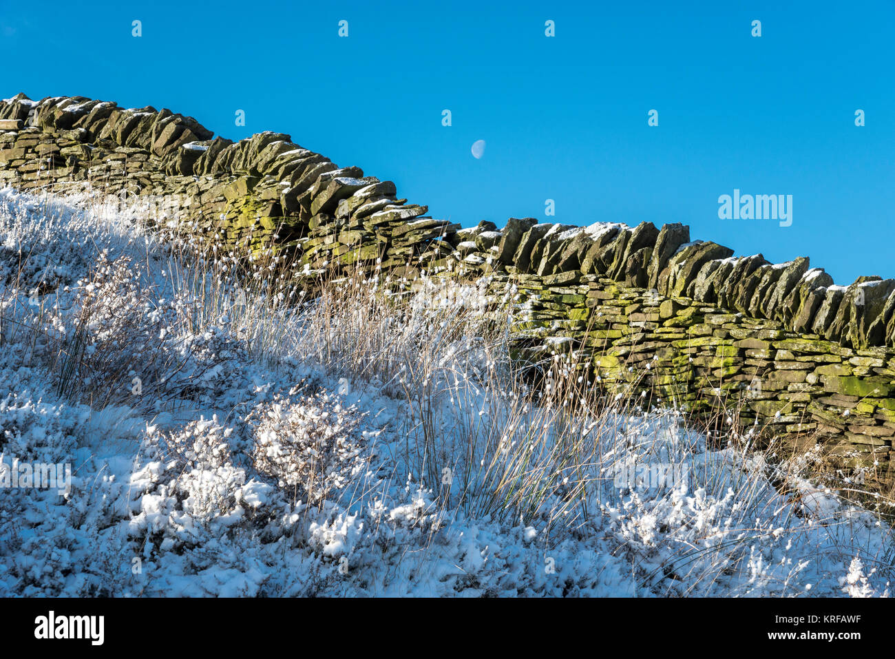 La luna in un cielo blu chiaro su un nevoso inverno mattina il Peak District, Derbyshire, in Inghilterra. Foto Stock