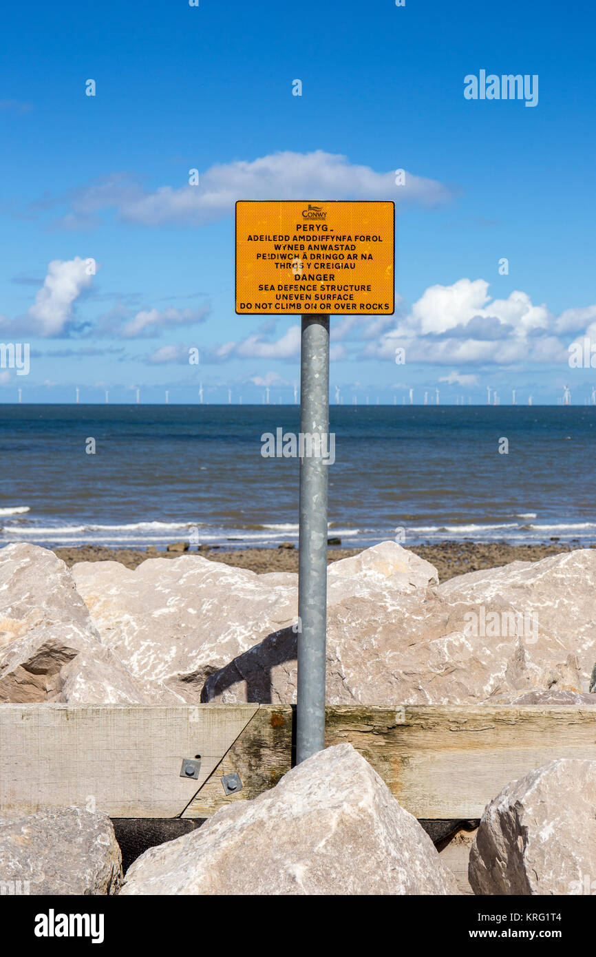 Avviso di pericolo di segno per la difesa del mare struttura superficiale irregolare. Non salire sulla o sulle rocce vicino a Llanddulas North Wales UK Foto Stock