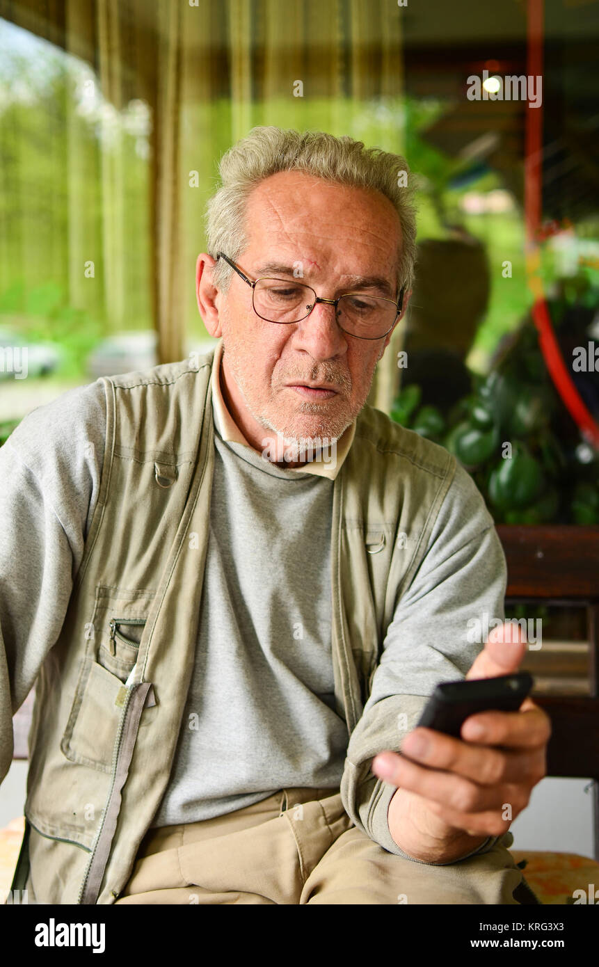 La conversazione è finita - uomo più anziano ha appena riagganciato, guardando il telefono cellulare dopo alcune cattive notizie Foto Stock