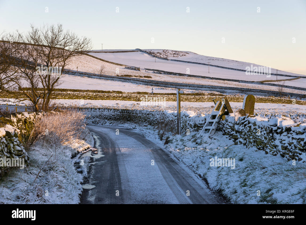 Icy country road e il paesaggio innevato in Inghilterra settentrionale su un nitido inverno mattina. Foto Stock