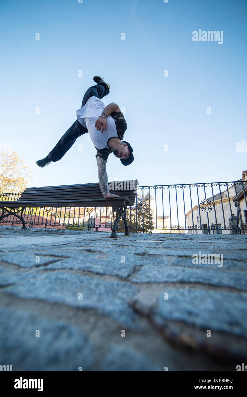 Giovane uomo facendo handstand su una panchina in strada mentre fa parkour. Foto Stock