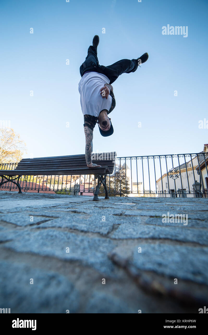 Giovane uomo facendo handstand su una panchina in strada mentre fa parkour. Foto Stock