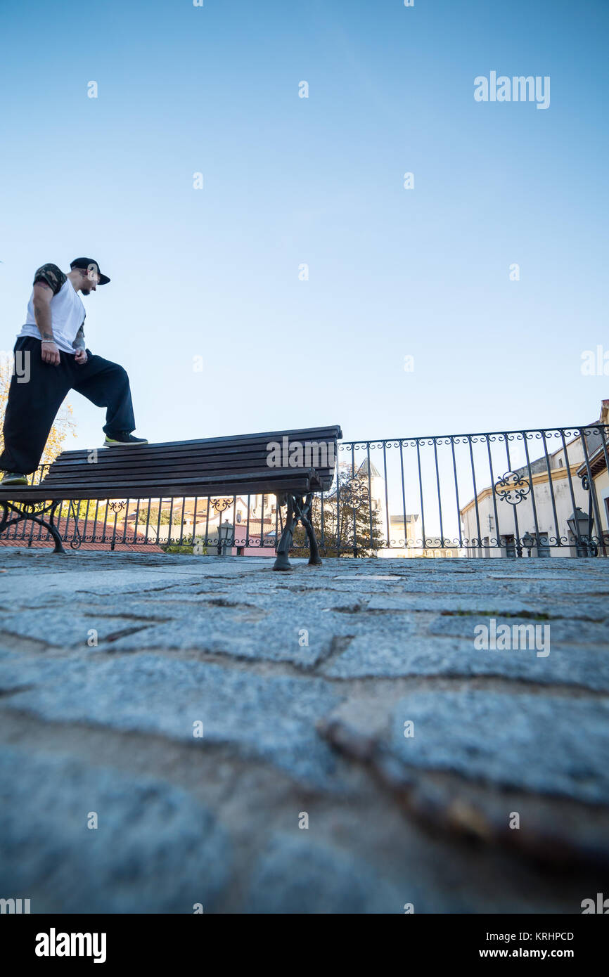 Giovane uomo guardando l'orizzonte appoggiato su una panchina in strada mentre fa parkour. Foto Stock