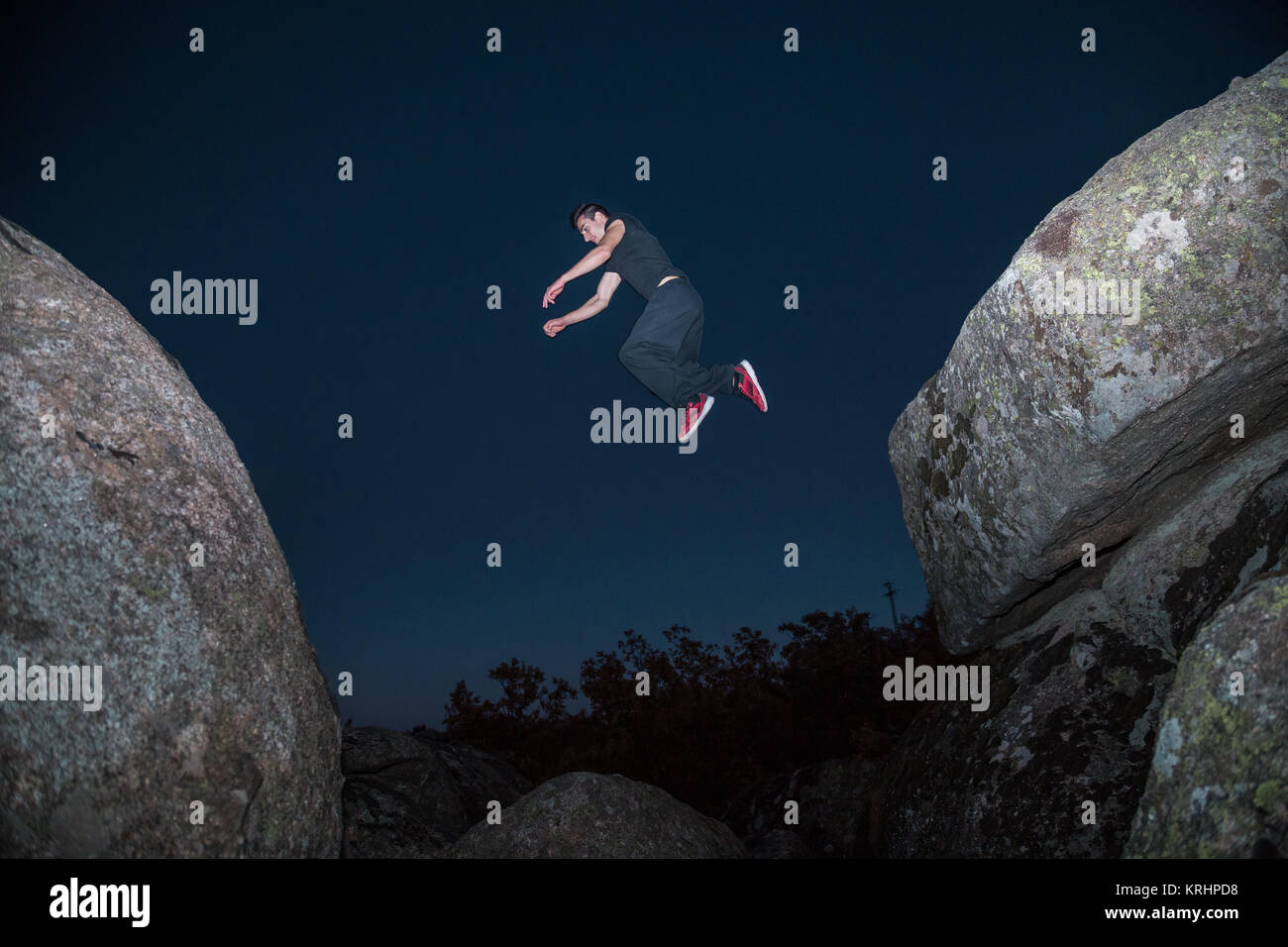 Da sotto vista di uomo sportivo saltando di roccia in roccia facendo parkour nella notte oscura. Foto Stock