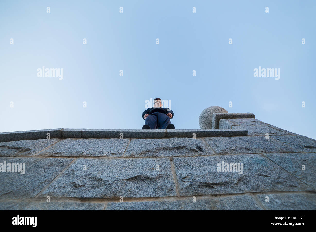 Giovane uomo in piedi sulla sommità di un muro di sporgersi a guardare il terreno mentre si fa parkour. Foto Stock