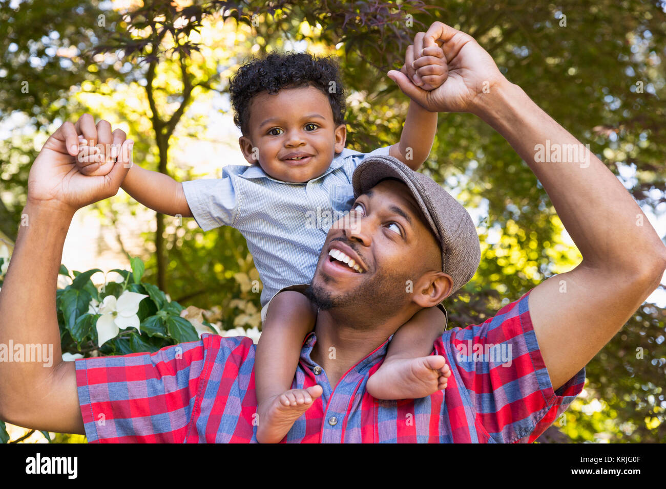 Sorridente razza mista padre bambino portando figlio sulle spalle Foto Stock