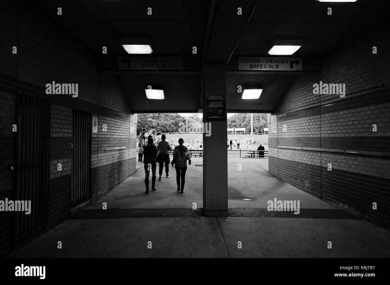 Passaggio per lo sport ovale con sagome di persone a piedi,. Corridoio con pareti di mattoni e luci a soffitto ad un'arena sportiva. Foto in bianco e nero o Foto Stock