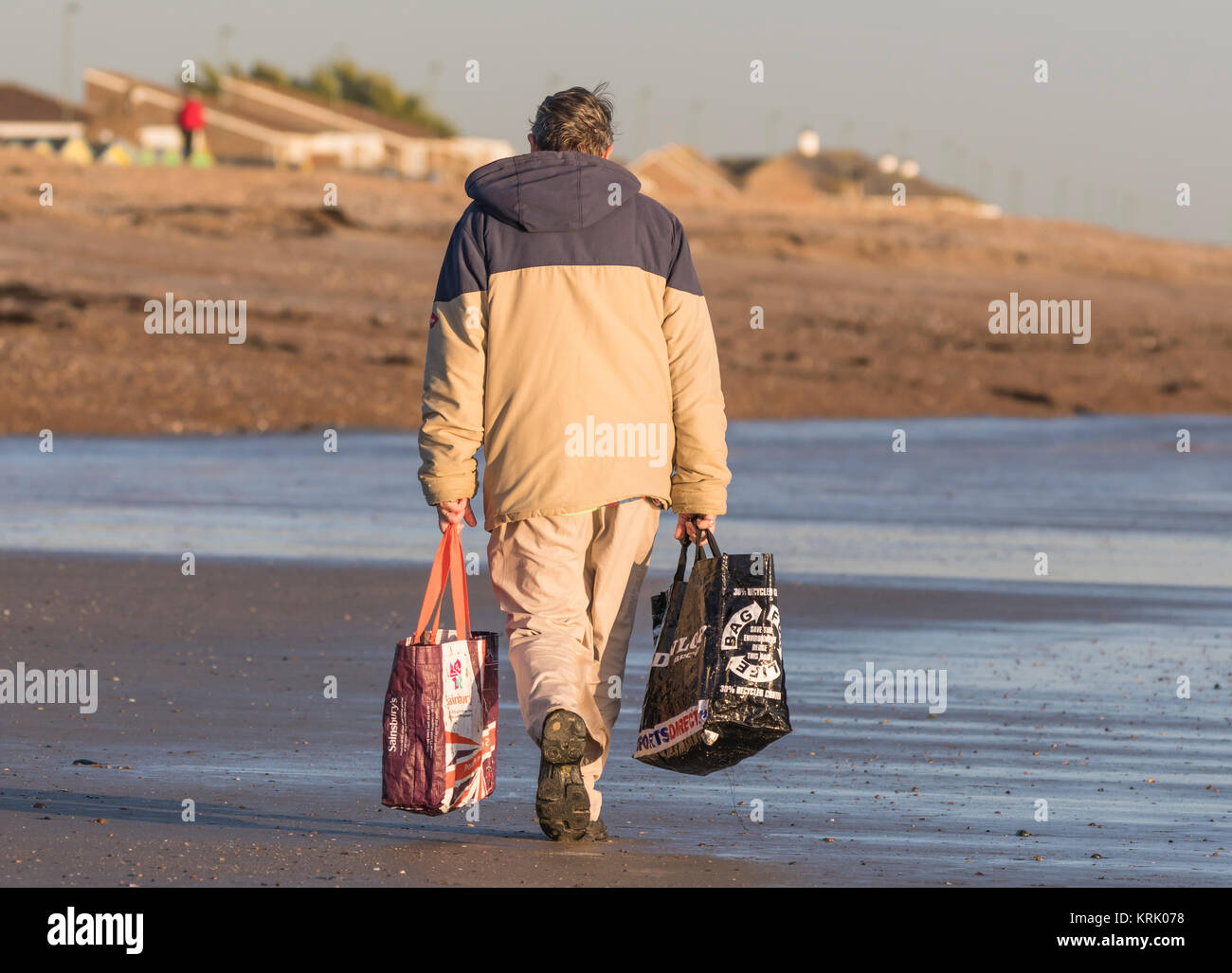 Uomo che cammina su una spiaggia il trasporto delle borse della spesa nel Regno Unito. Foto Stock