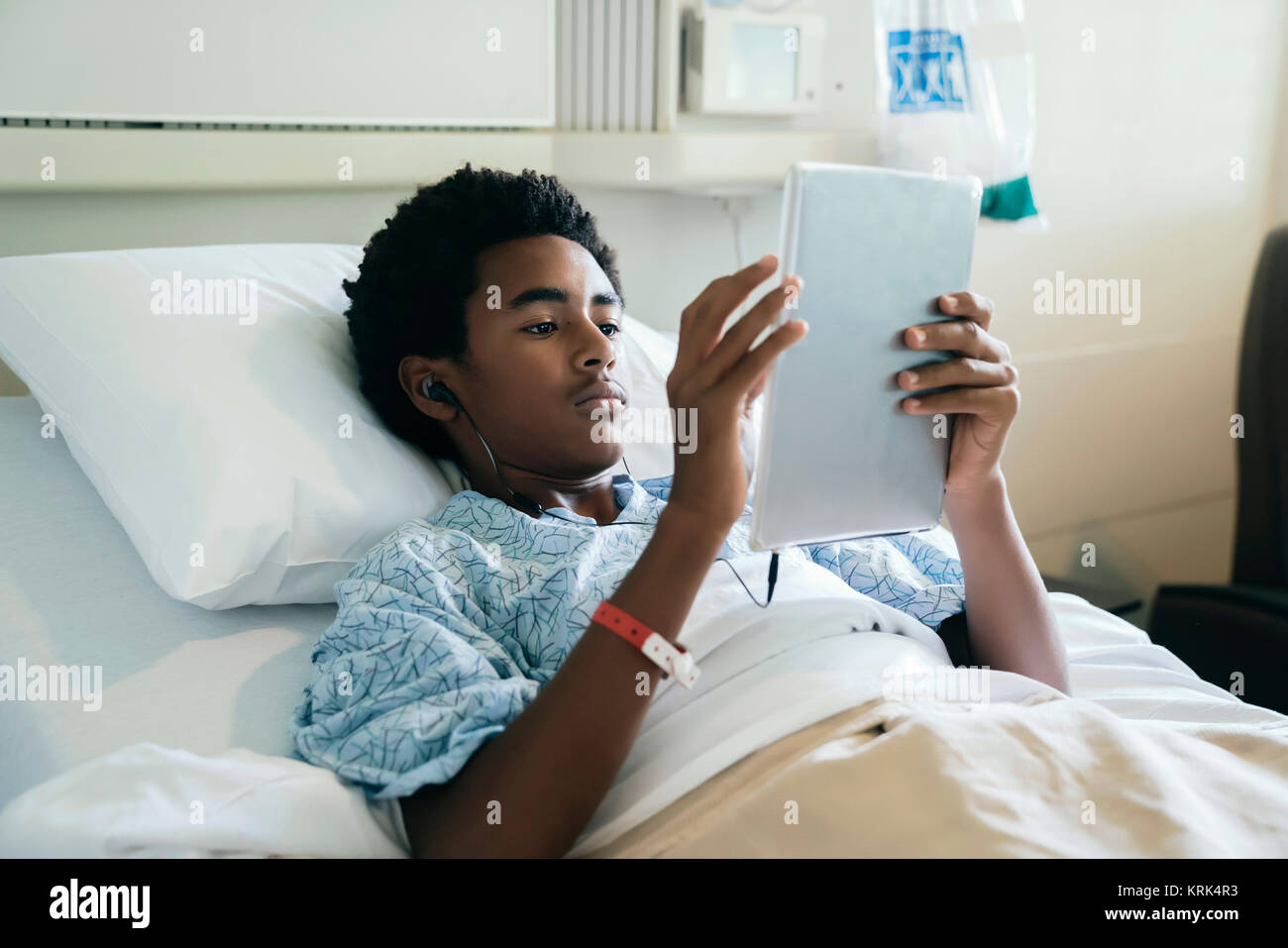 Black Boy nel letto di ospedale ascoltando la tavoletta digitale Foto Stock