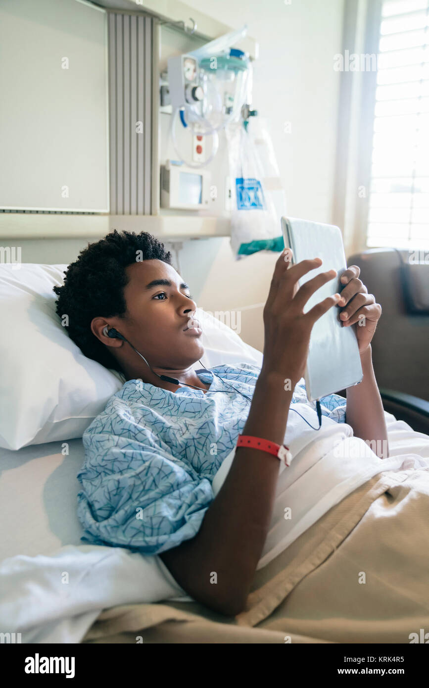 Black Boy nel letto di ospedale ascoltando la tavoletta digitale Foto Stock