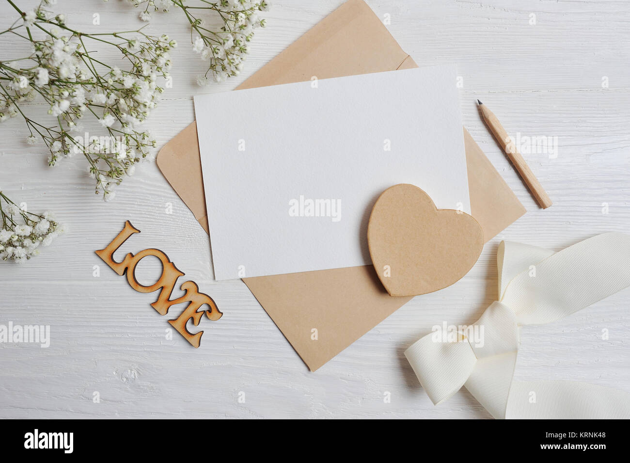 Mock up lettera con un amore scatola a forma di cuore giace su una tavola di legno tavolo bianco con gypsophila fiori, un biglietto di auguri per il giorno di San Valentino con Foto Stock
