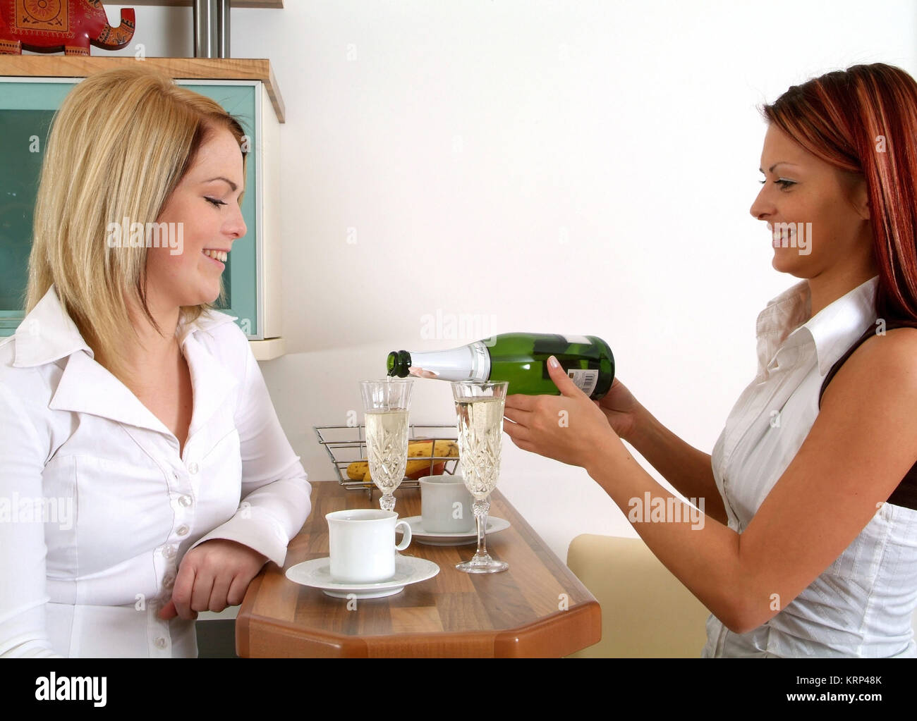 Zwei junge Frauen trinken gemeinsam Sekt an der Kuechenbar - due giovani donne a bere vino spumante Foto Stock