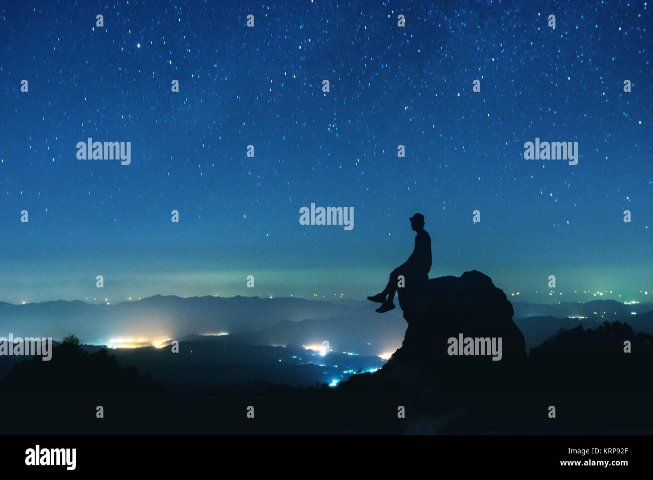 L uomo si siede sul big rock sul cielo notturno sullo sfondo Foto Stock