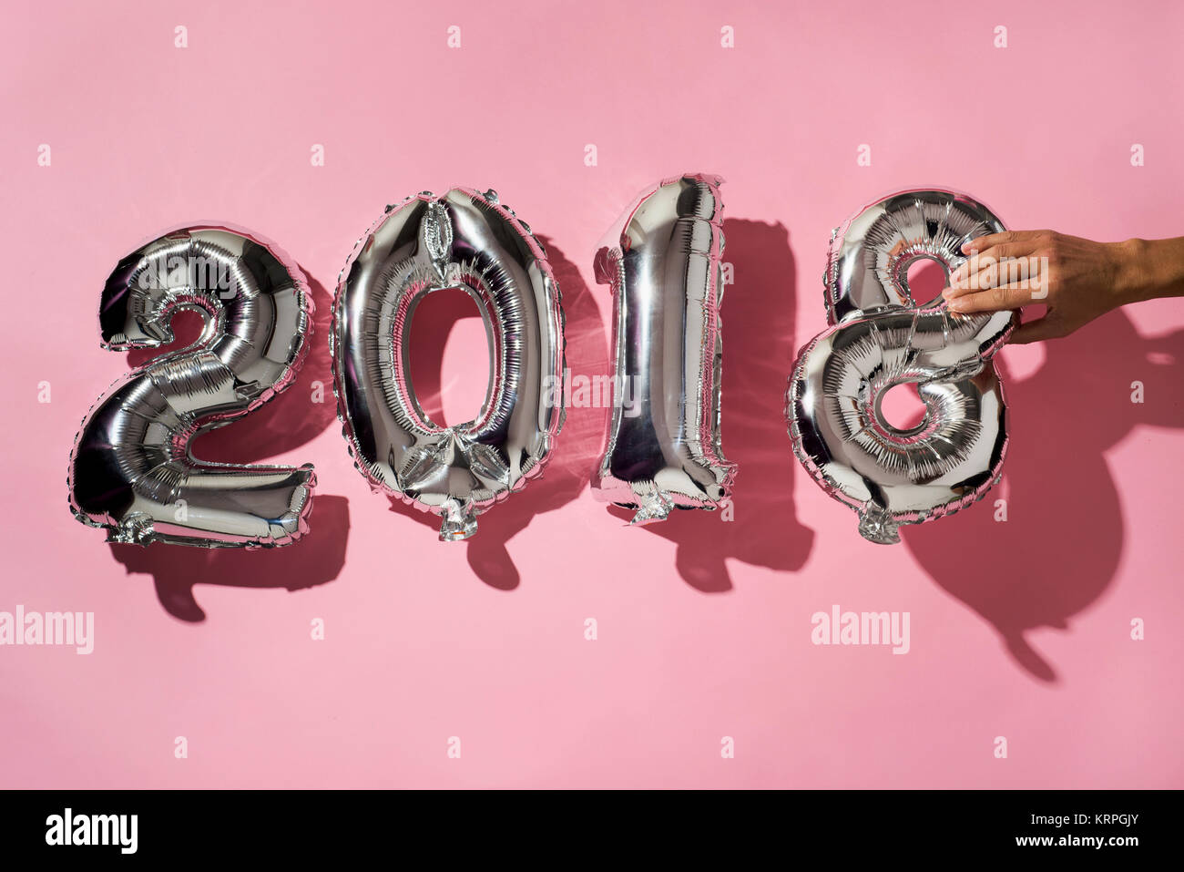 Giovane uomo formando il numero 2018, come l'anno nuovo con numero argenteo di palloncini sagomati, contro un sfondo rosa Foto Stock