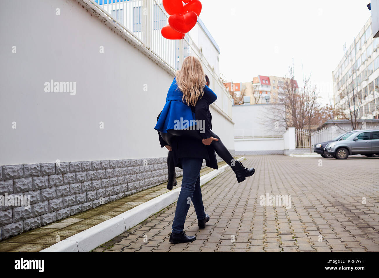 Ragazza piggyback sul ragazzo con cuore rosso palloncini sulla strada. Foto Stock