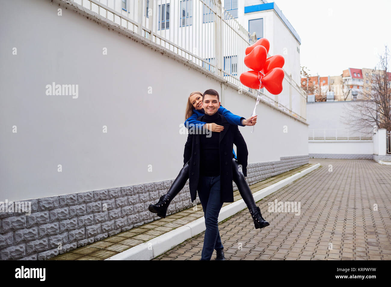 Ragazza piggyback sul ragazzo con cuore rosso palloncini sulla strada. Foto Stock