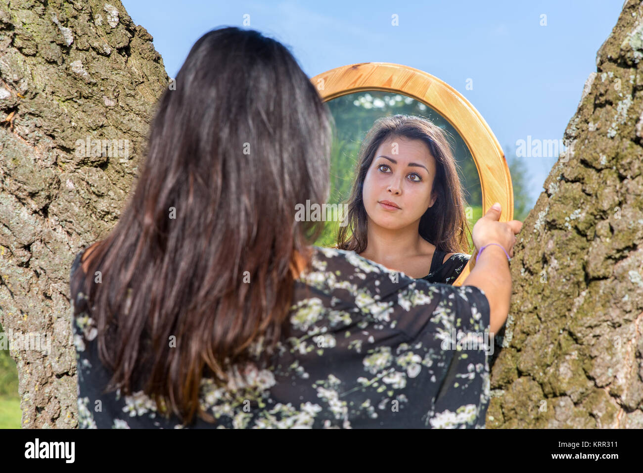 Giovane donna cercando in mirror tra la betulla tronchi di alberi Foto Stock