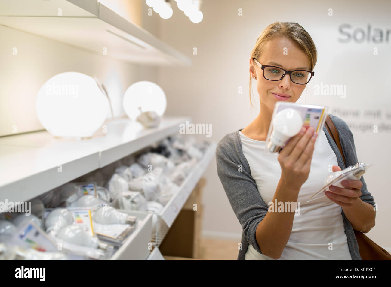Illuminazione a basso consumo scelta: piuttosto, giovane donna holding e la scelta di un diodo LED lampadina per la sua lampada in DIY department store Foto Stock