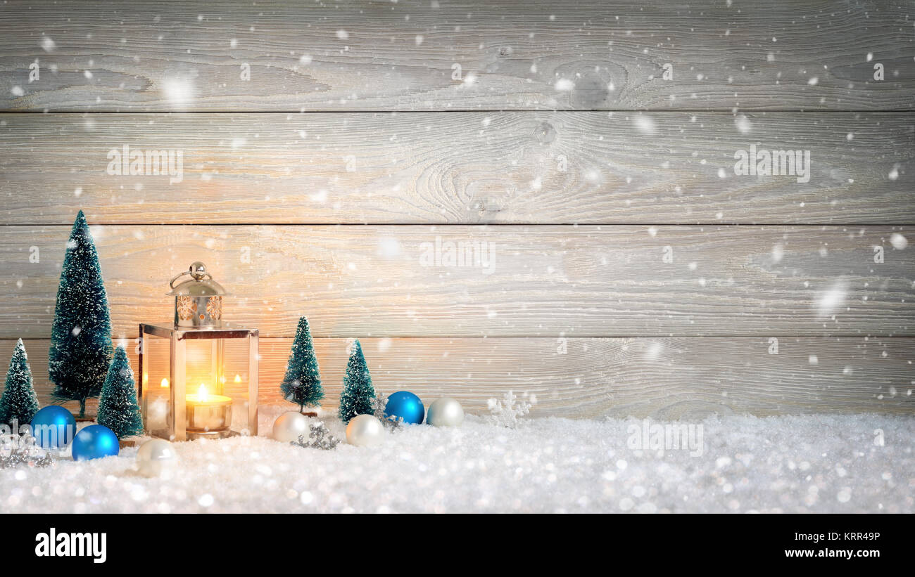 Sfondo di natale con tavola di legno, caduta di neve, una candela che brucia in una lanterna e ornamenti Foto Stock