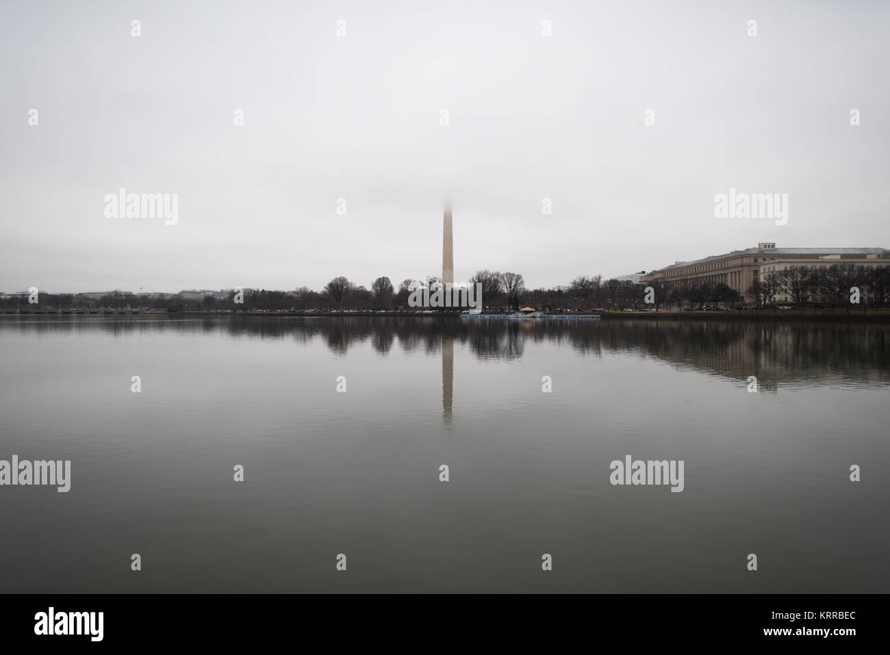 WASHINGTON DC - il monumento a Washington si riflette nelle acque calme del bacino delle maree in un giorno nebbioso e coperto. I ciliegi circostanti sono nudi, indicando l'inverno o l'inizio della stagione primaverile prima che i fiori emergano. La parte superiore dell'obelisco di marmo, che onora il primo presidente degli Stati Uniti George Washington, è oscurata da nuvole basse. Foto Stock