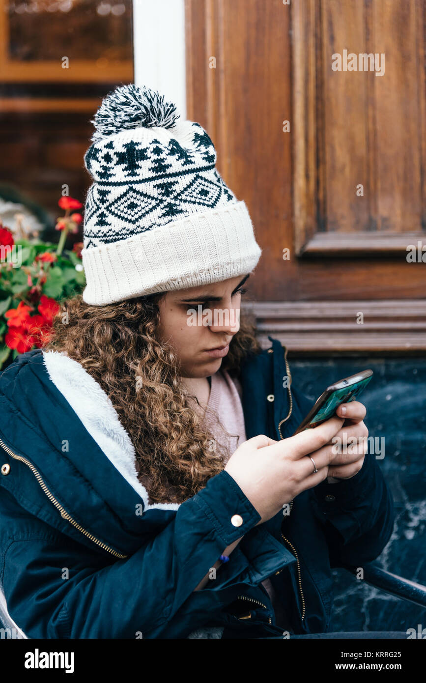 Ragazza adolescente in knit hat texting con un telefono cellulare Foto Stock