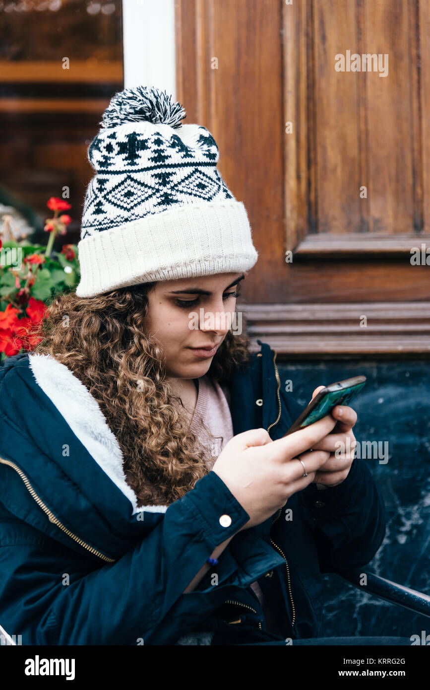 Ragazza adolescente in knit hat texting con un telefono cellulare Foto Stock