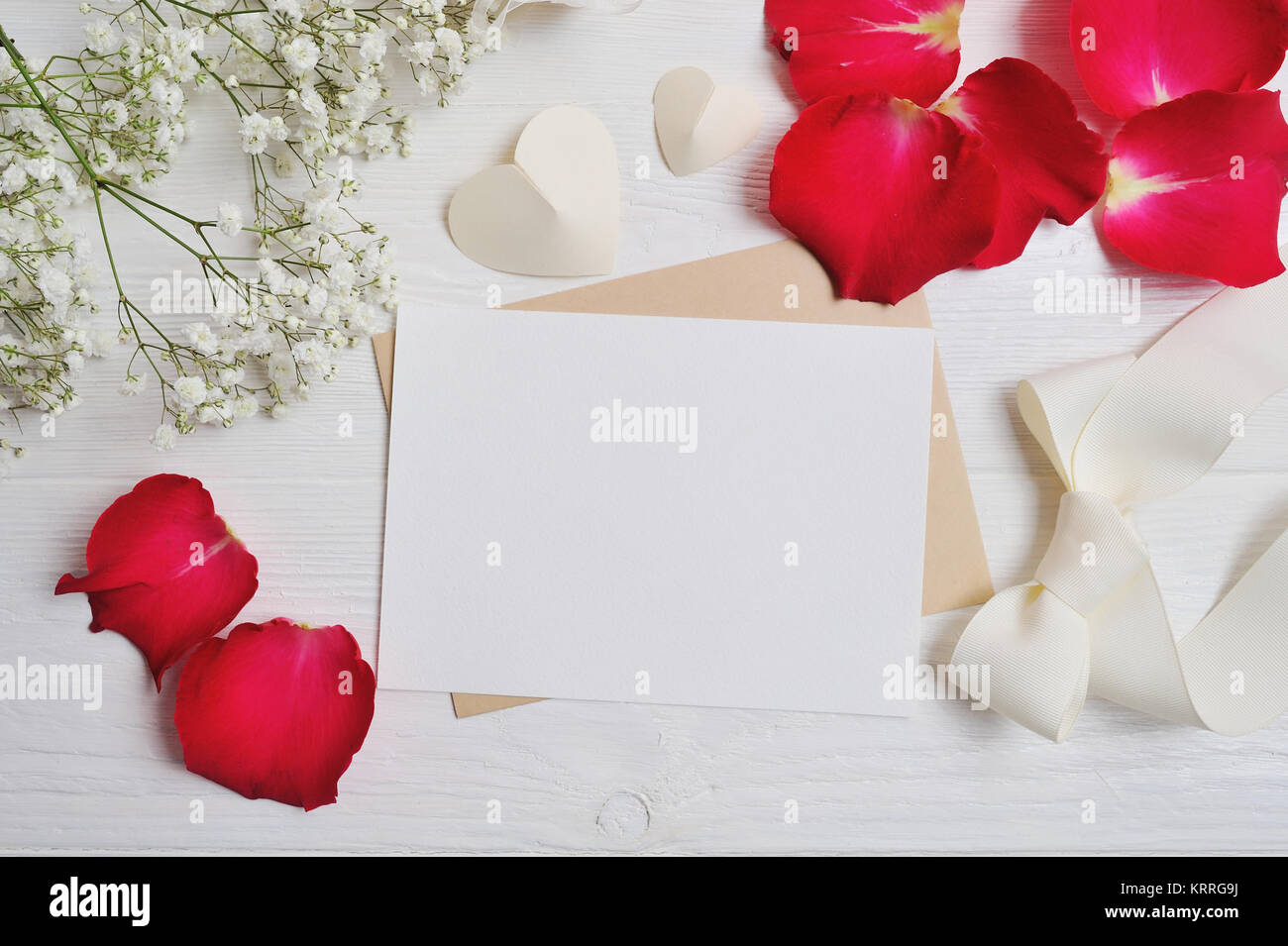 Mockup composizione di fiori da gypsophila con un cuore lettera con il rosso dei petali di rosa sul bianco sullo sfondo di legno. Il giorno di San Valentino. Appartamento laico, vista dall'alto wi Foto Stock