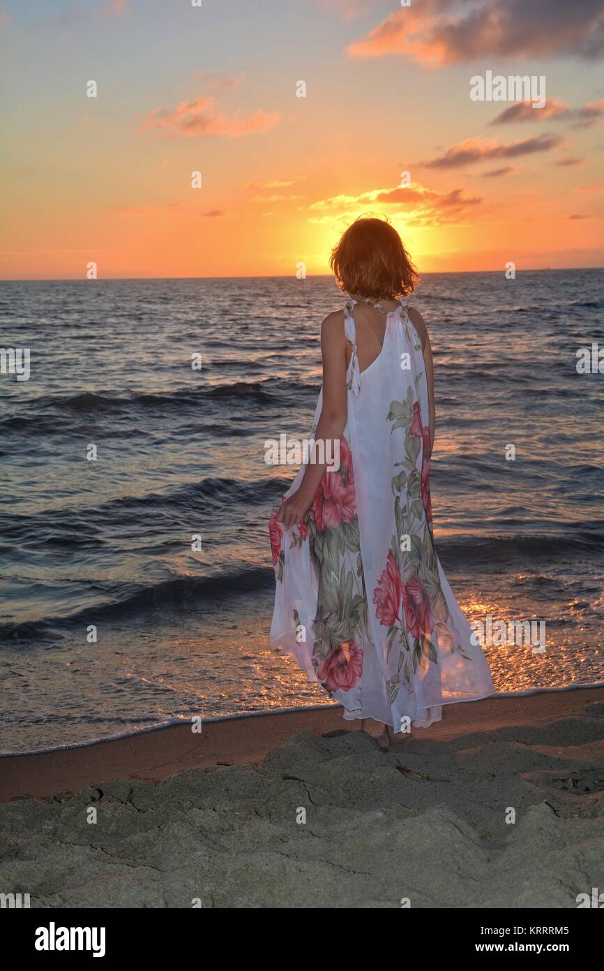 Ragazza in abito lungo in piedi sul mare spiaggia al tramonto Foto stock -  Alamy