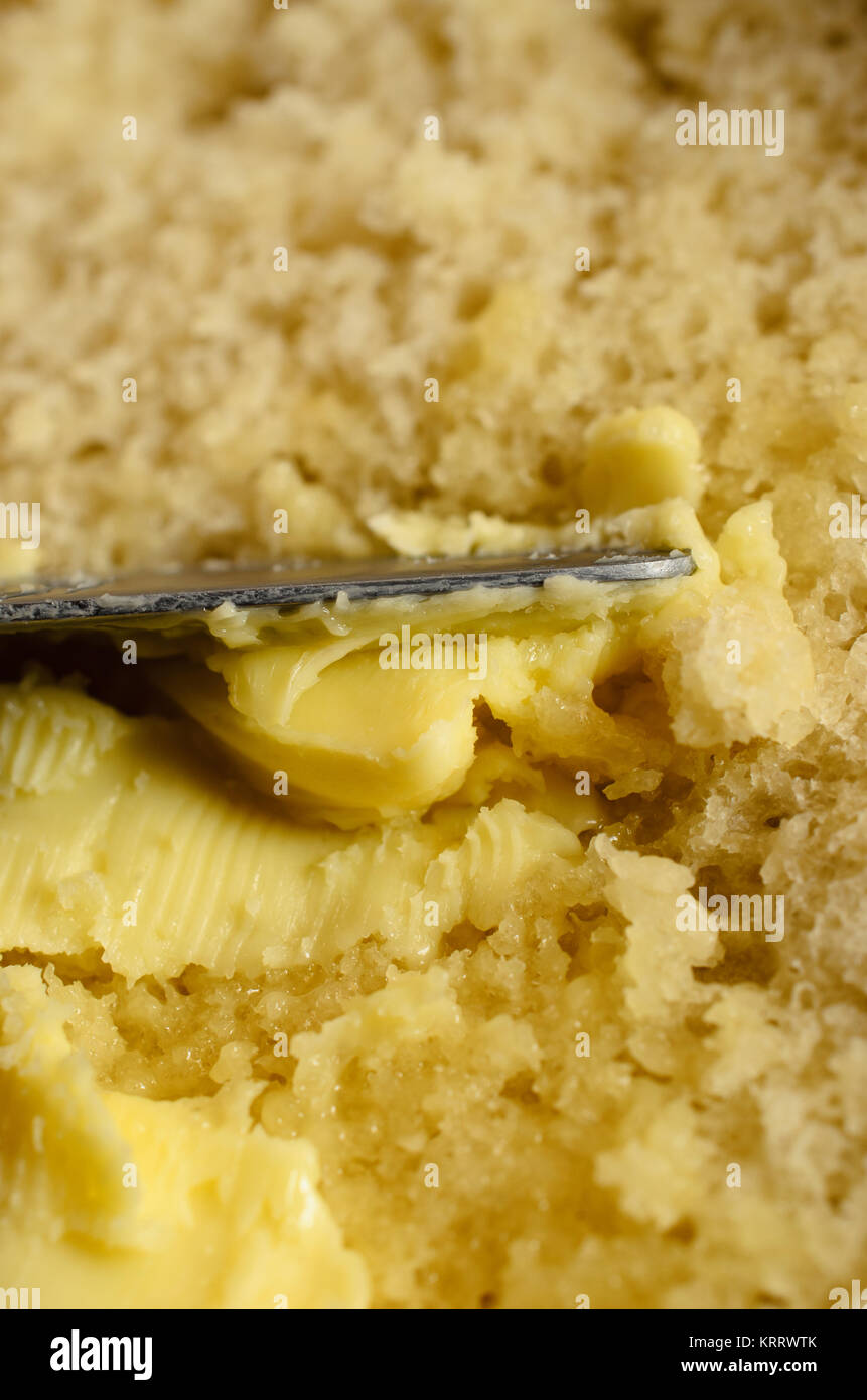 Close up di spalmatura a coltello di burro fresco caldo fetta di pane. Foto Stock