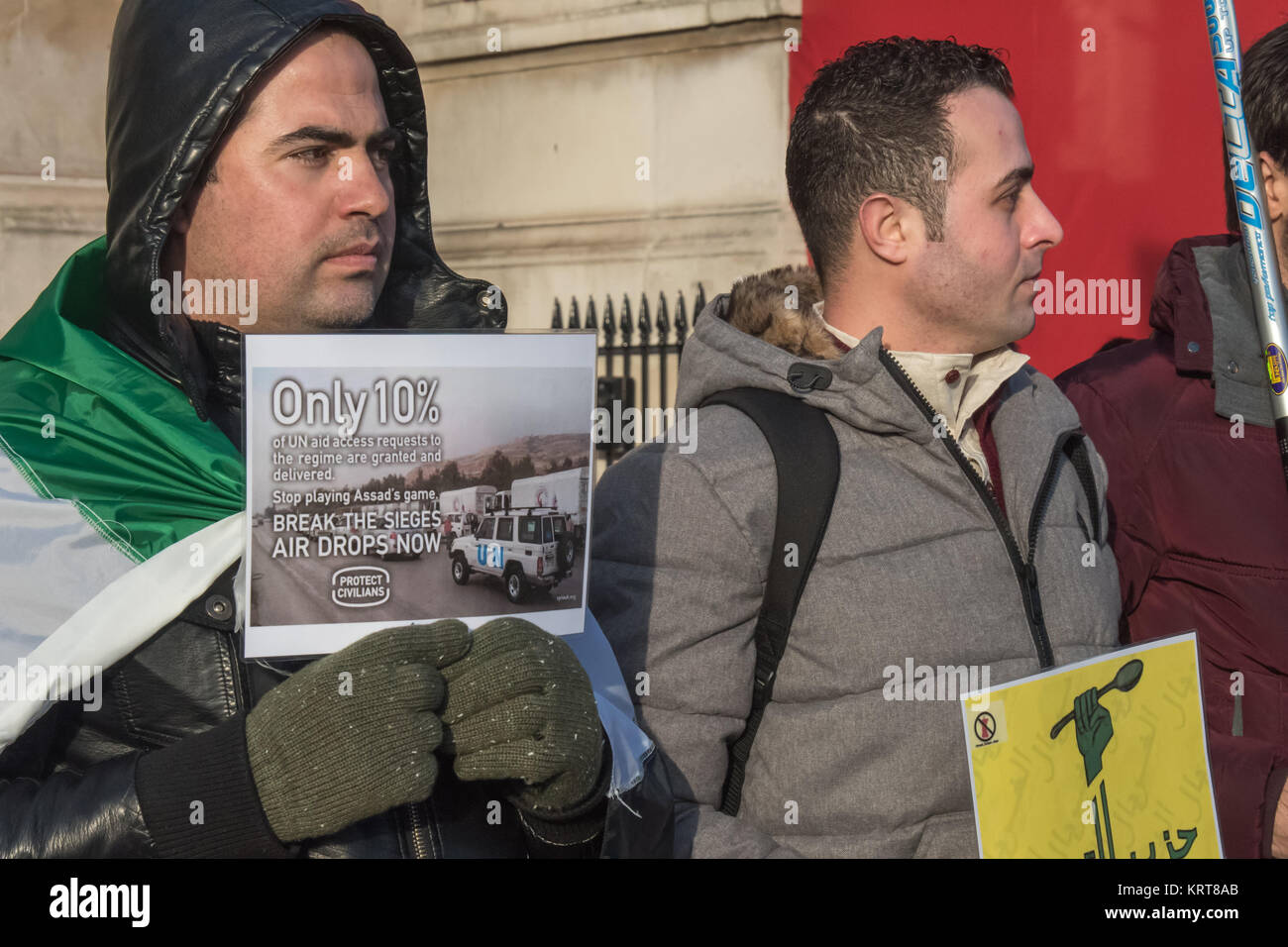 Un uomo con un libero bandiera siriana detiene un poster callinf per le Nazioni Unite per fermare la riproduzione di Assad di gioco e rompere il siriano assedi da aria scende fo cibo ora al 'Cibo non bombe' protestare in Trafalgar Square. Foto Stock