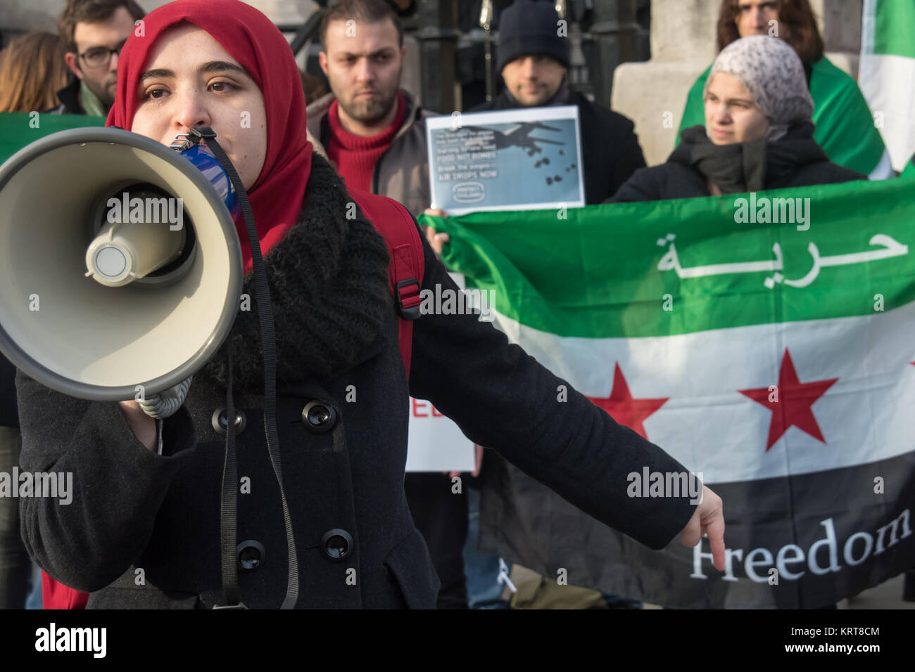 Una donna in un rosso headscart parla al 'Cibo non bombe' per la Siria in Trafalgar Square di fronte a forze democratiche libertà bandiera, il suo dito davanti la parola "libertà" su di esso. Foto Stock