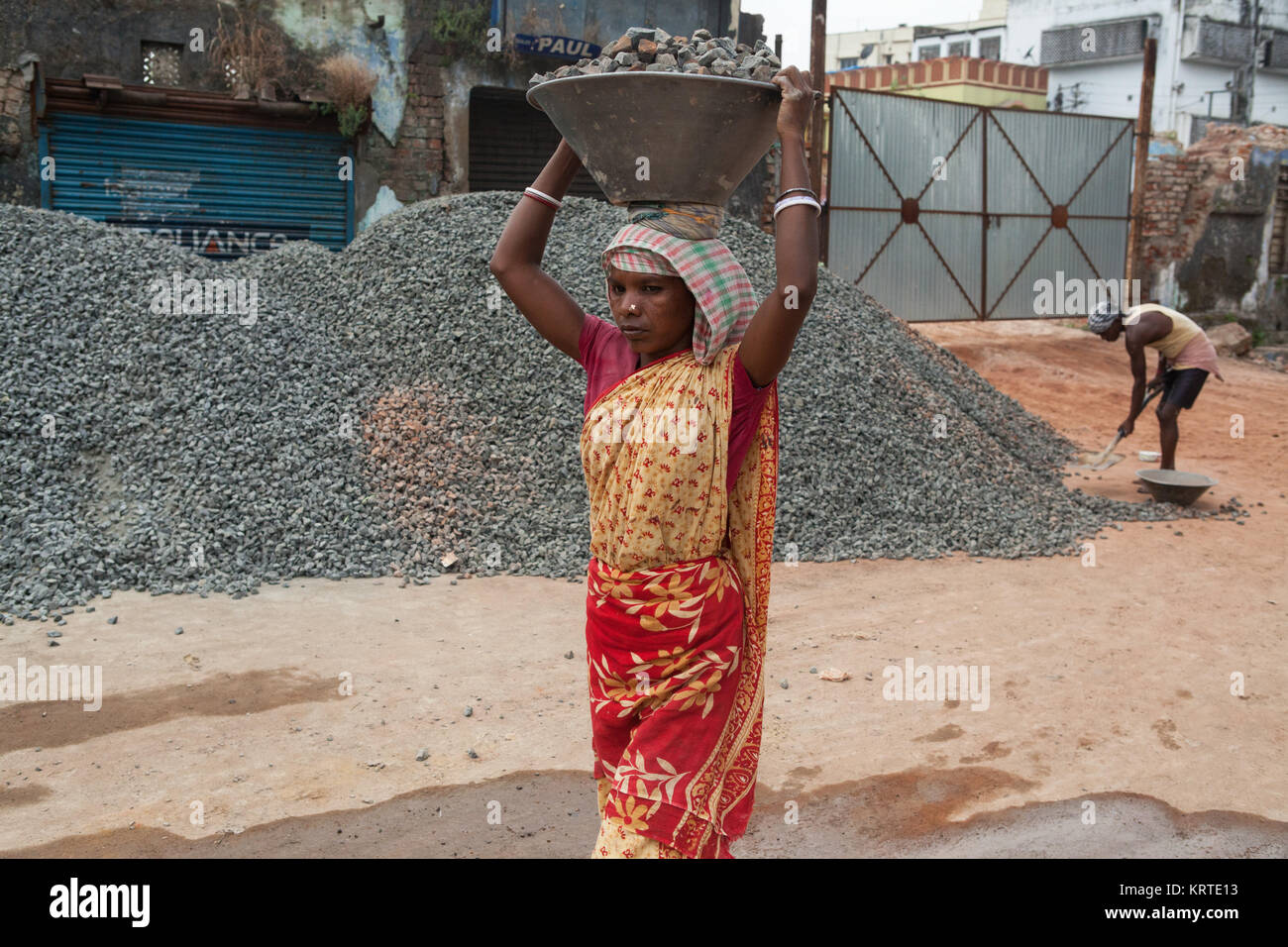 Una donna che porta un vassoio di trucioli di pietra su un sito di costruzione in Asansol, India Foto Stock