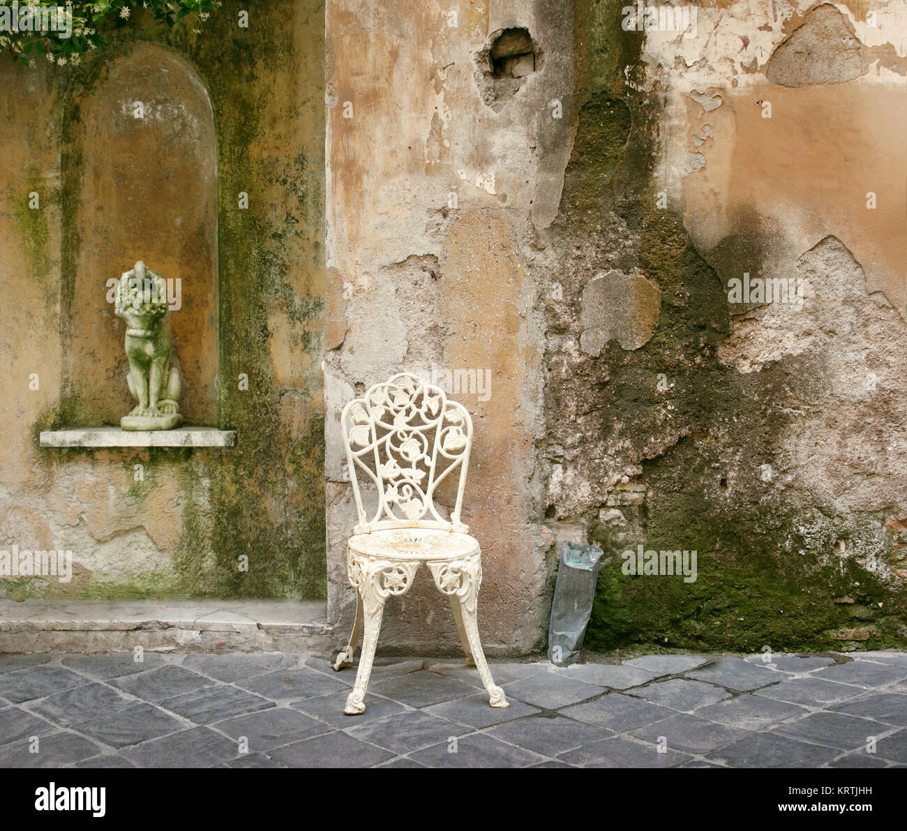Una caratteristica e decadente angolo di un vecchio muro cadente con un vecchio ferro battuto sedia e una piccola statua Foto Stock