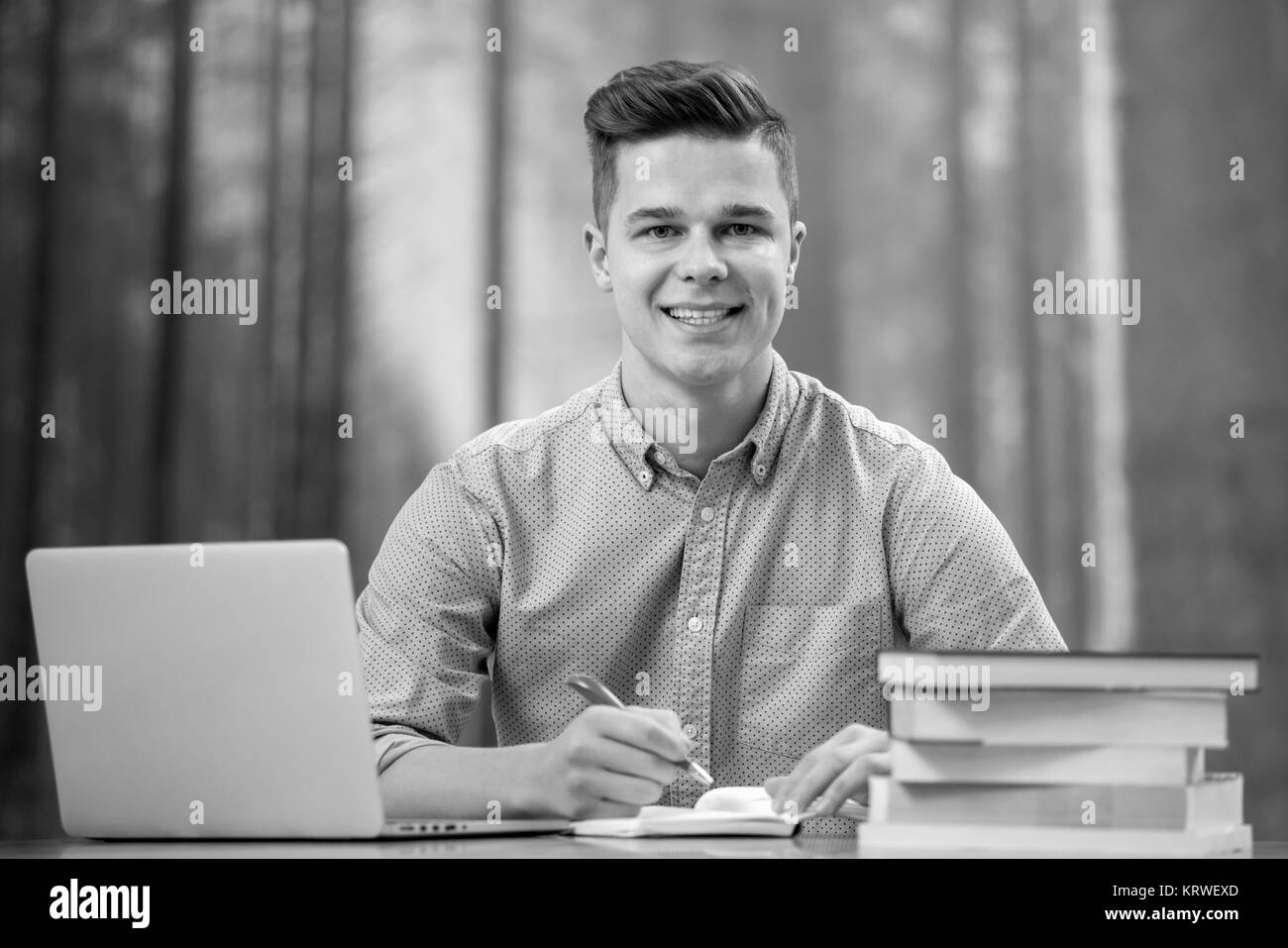 Un giovane e attraente uomo utilizzando il suo telefono e computer portatile circondata con i libri Foto Stock