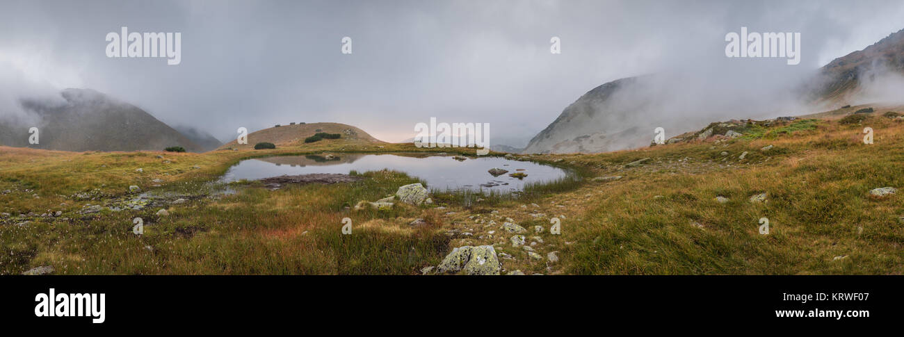 Piccolo Tarn con la nebbia in montagna al tramonto Foto Stock