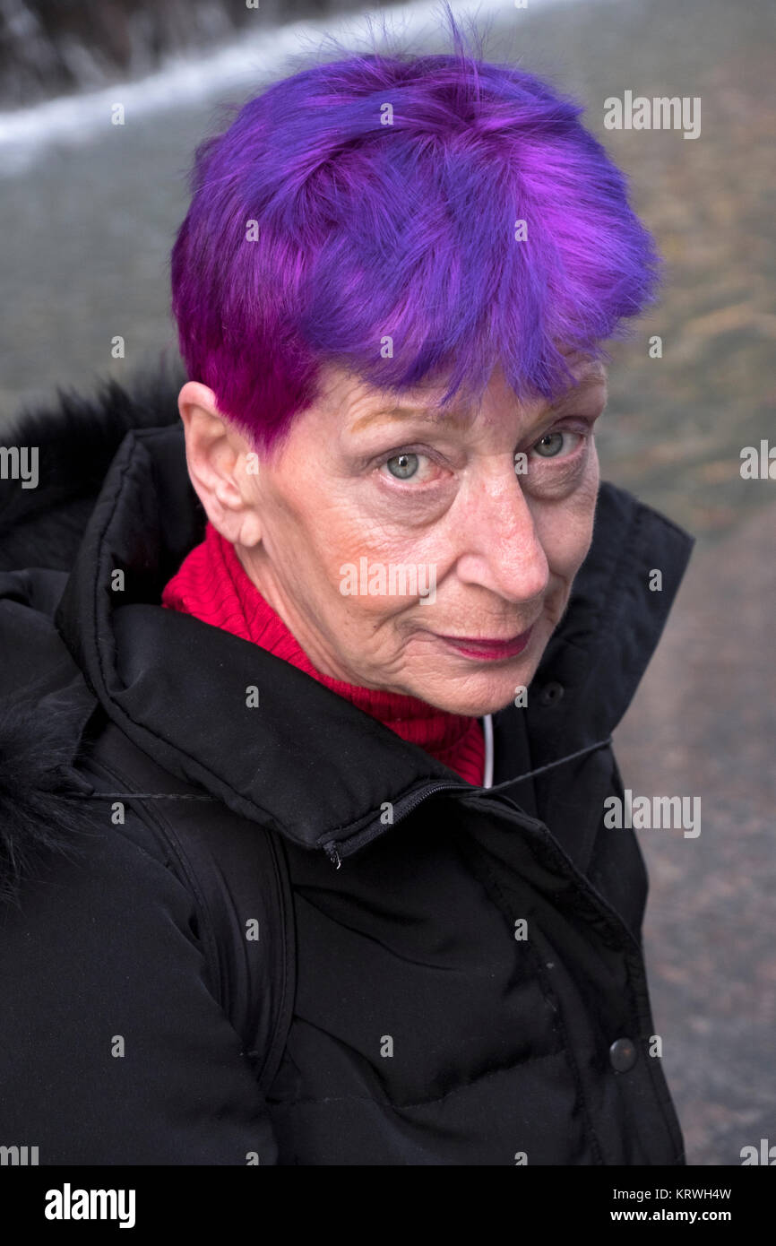 Poste ritratto di una donna attraente nel suo molto primi anni sessanta con giovanile viola e capelli rossi. In Midtown Manhattan, a New York City. Foto Stock